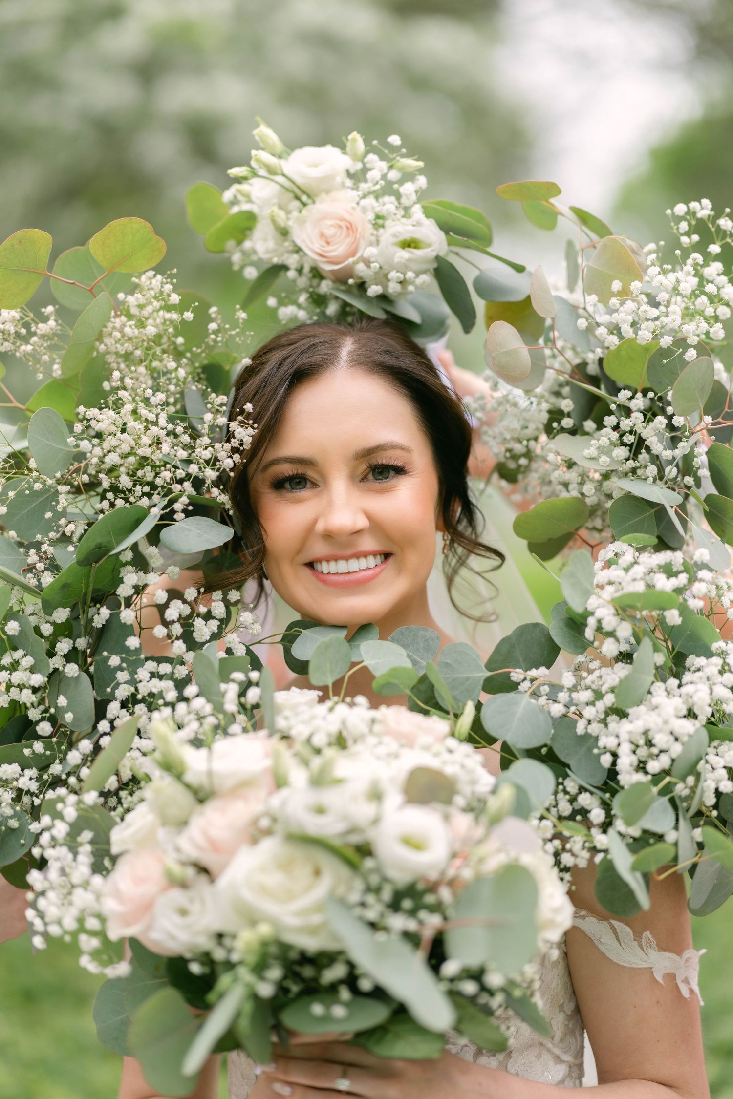 Smiling bride framed by eucalyptus and baby's breath wreath holding white and pink rose bouquet on wedding day.