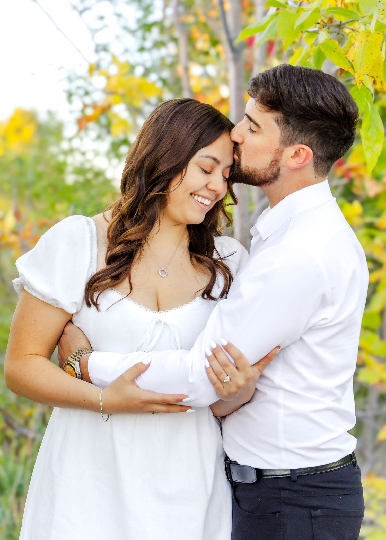 Intimate moment captured between couple in white outfits against autumn foliage.