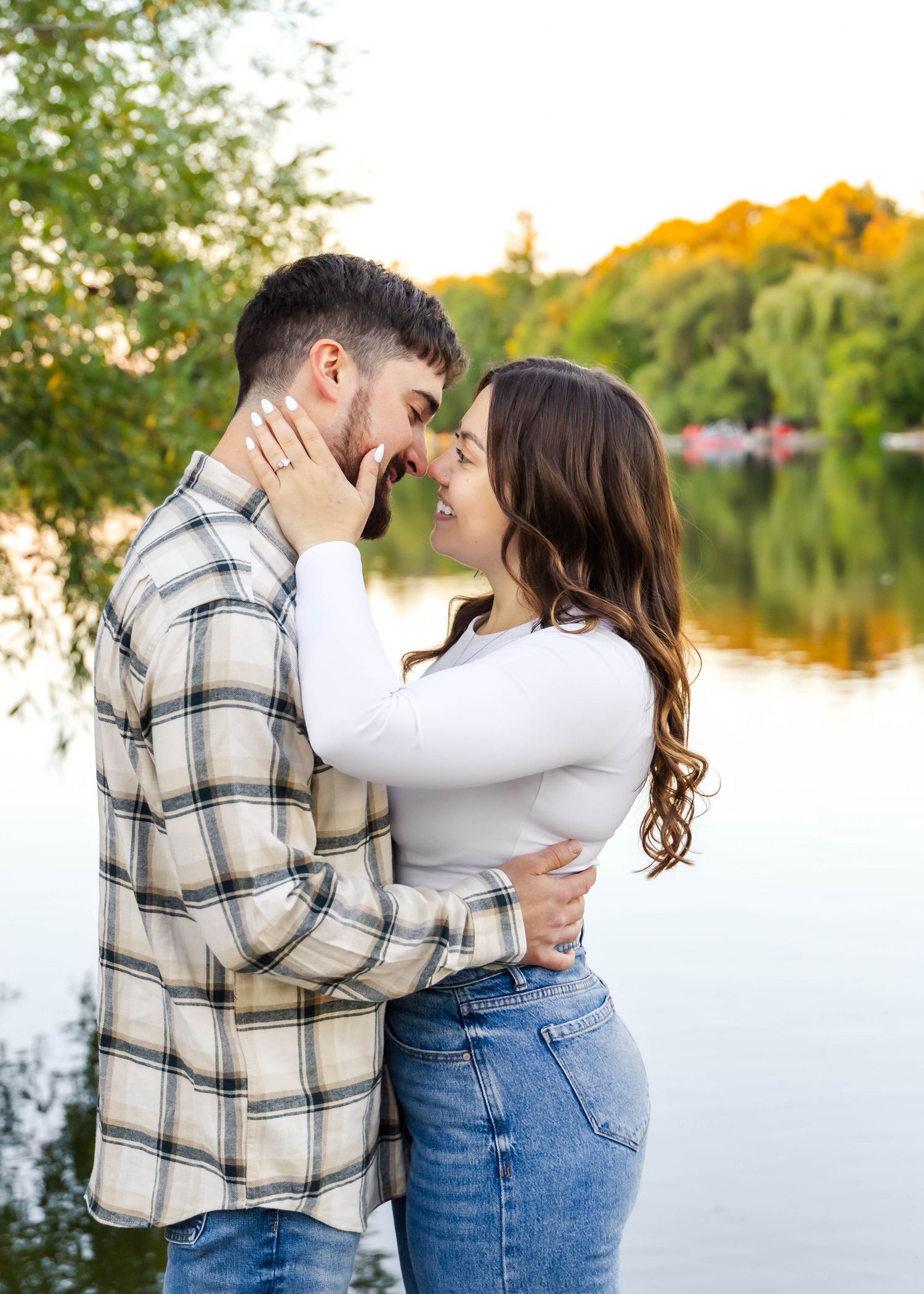 An affectionate couple sharing an intimate moment by a lake with fall colors in the background.