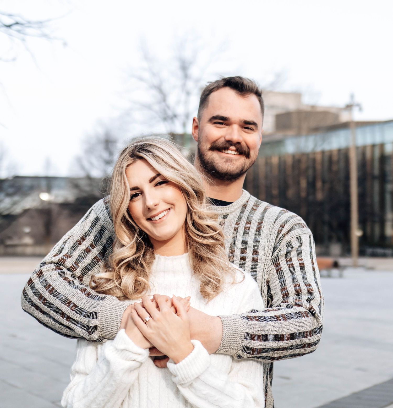 A happy couple wearing matching striped sweaters embraces and laughs together outdoors.