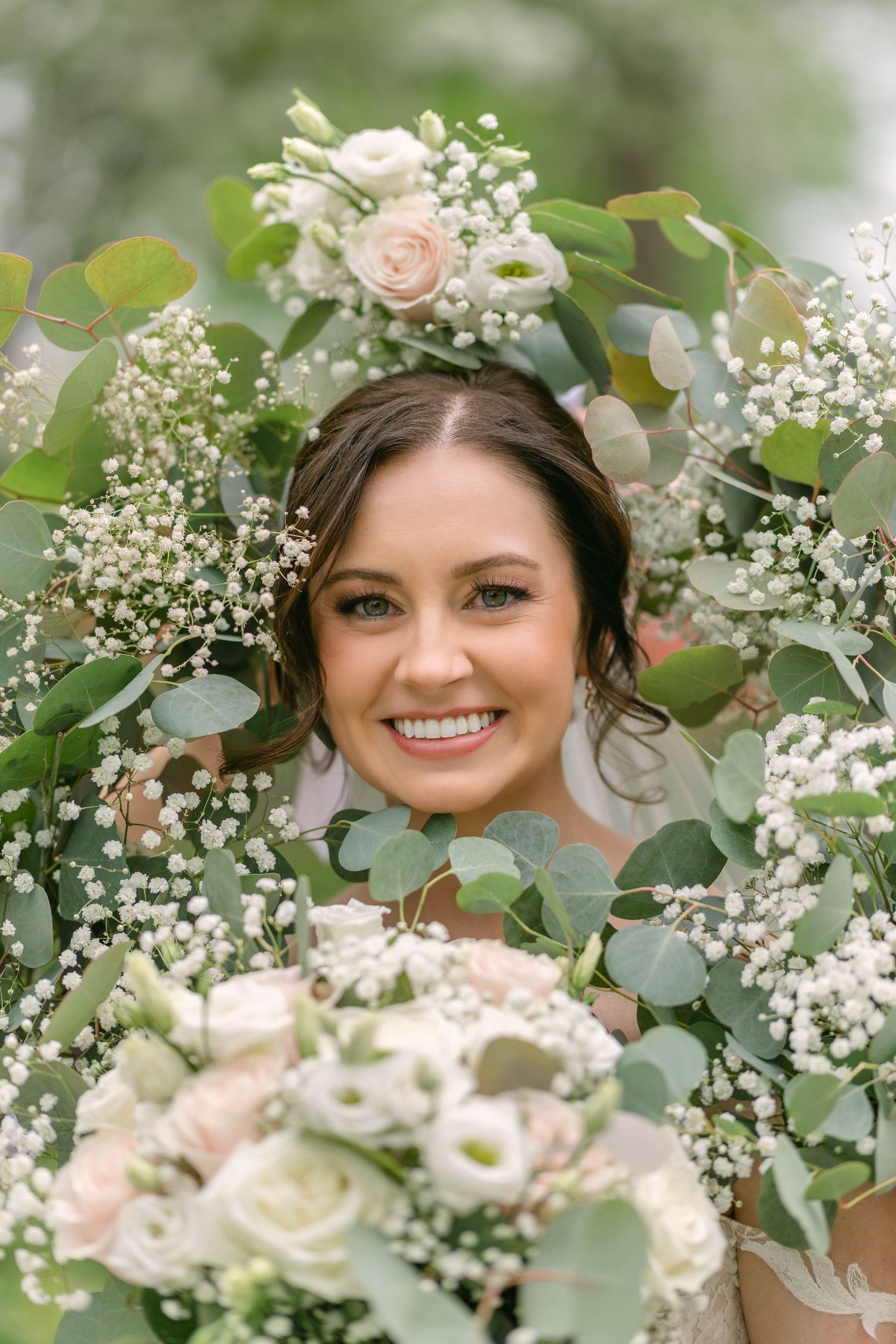 Radiant bride smiling through lush greenery and white floral bouquet with eucalyptus and baby's breath.