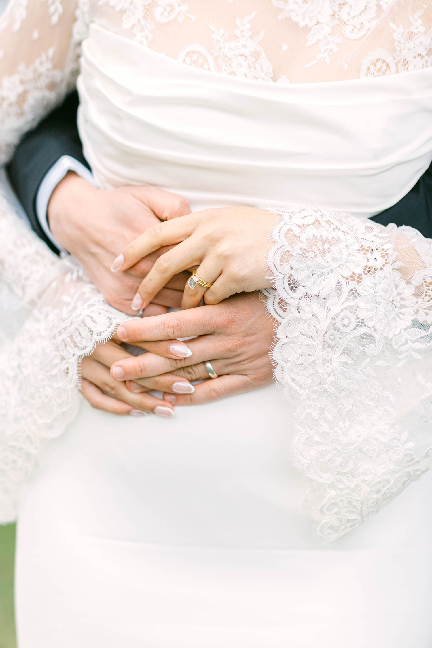Close-up of bride and groom hands with gold wedding rings, bride wearing elegant white lace dress.