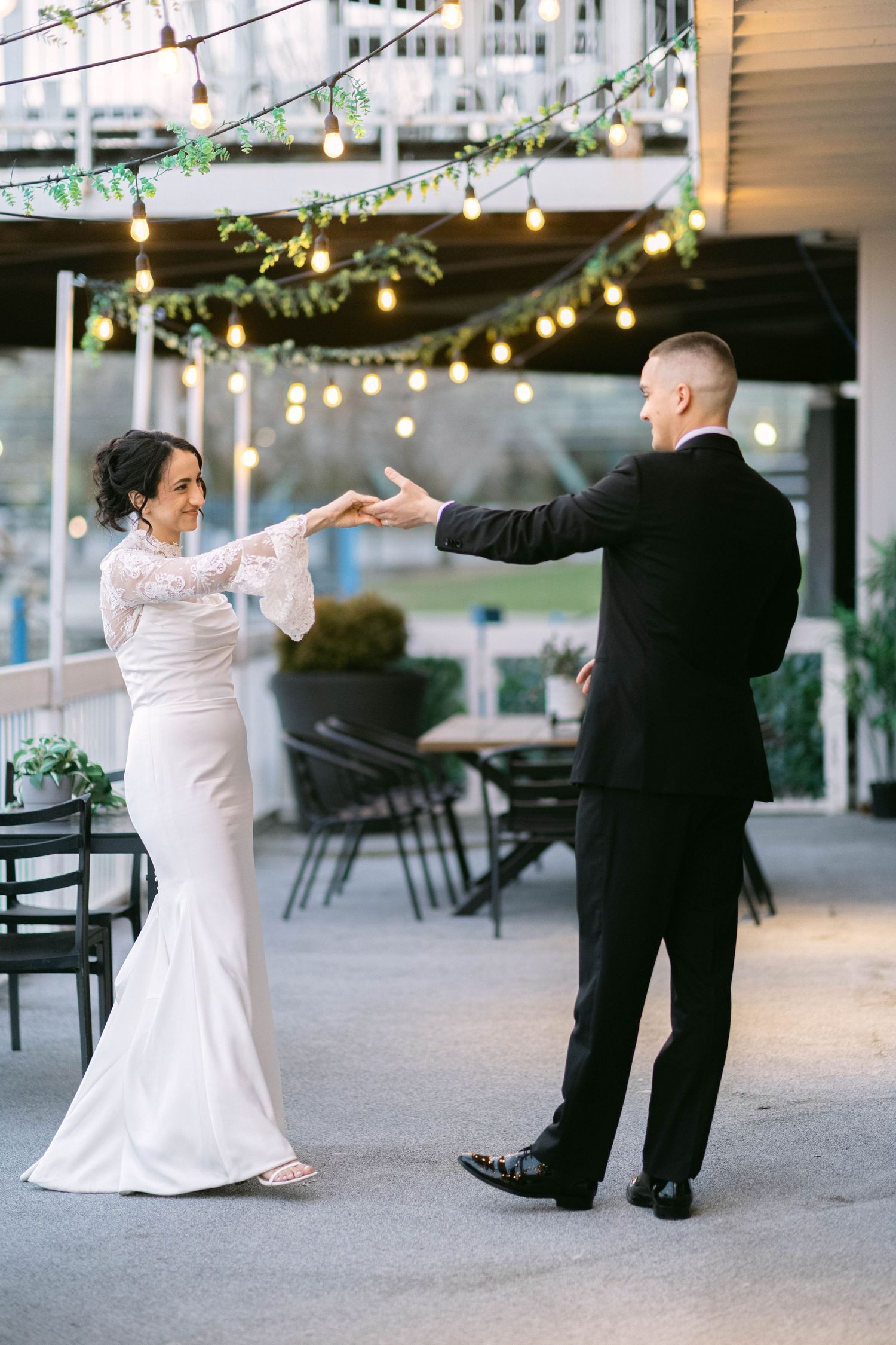 Bride and groom share a romantic first dance outdoors under warm string lights at an elegant wedding venue.