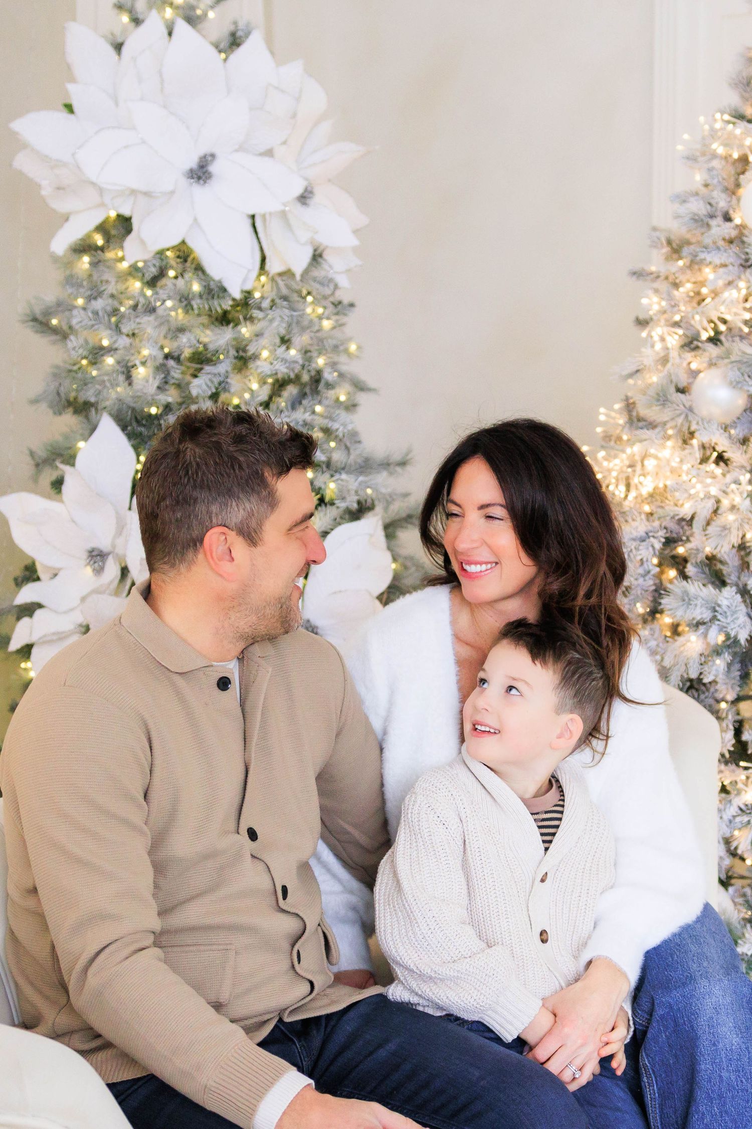 Family sitting together and laughing on couch near decorated Christmas tree.