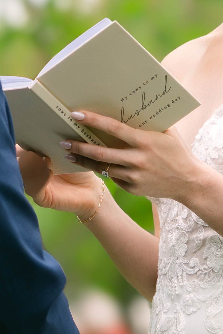 Bride reading wedding vows from a white booklet titled 'My Vows to My Husband' on her wedding day.