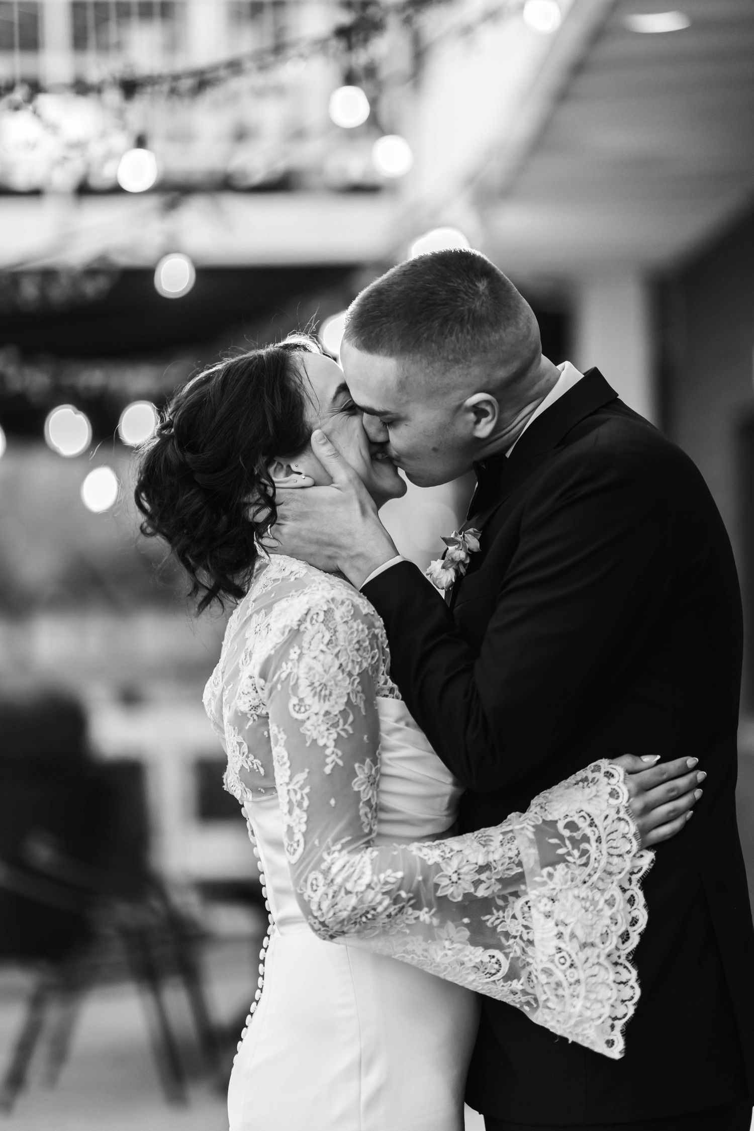 Black and white photo of a bride and groom sharing a romantic kiss at their wedding reception.