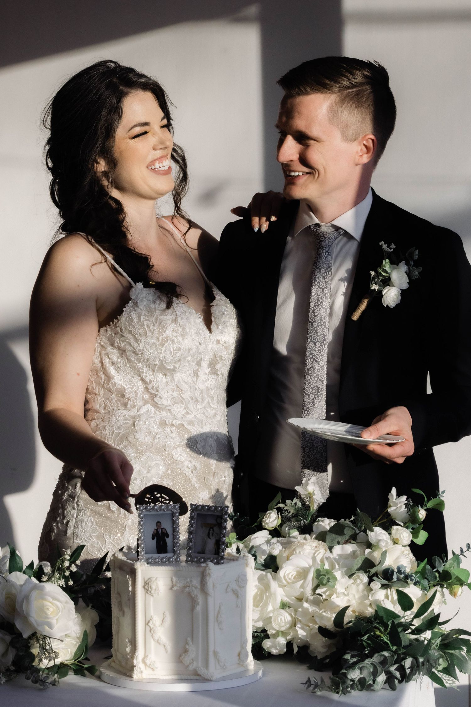 Couple shares cake tasting moment at their wedding reception with elegant white floral decor.