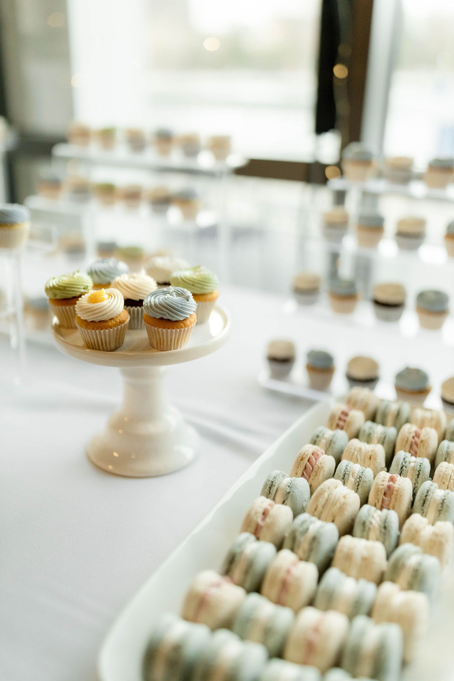 Elegant dessert table with pastel macarons and mini cupcakes on a white cake stand at a wedding reception.