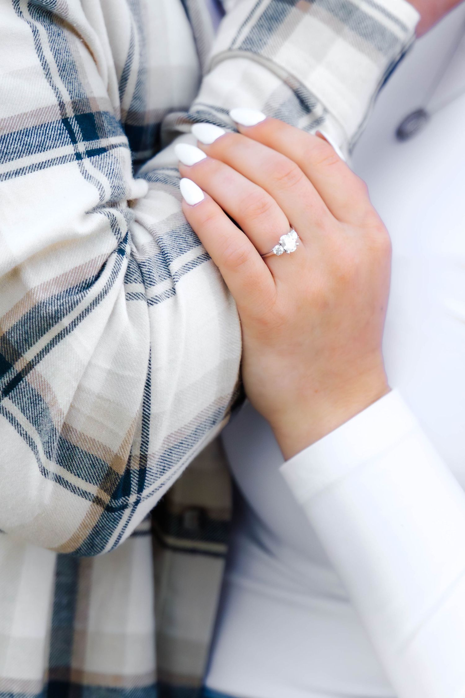 Close-up of hands showing engagement ring against plaid fabric.