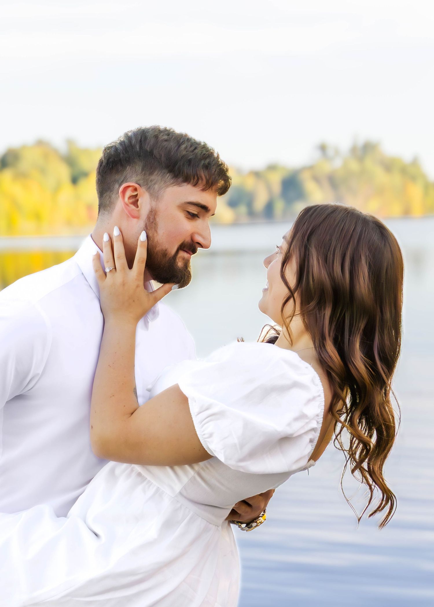 Romantic dip pose during lakeside photo session with water and autumn trees in background.