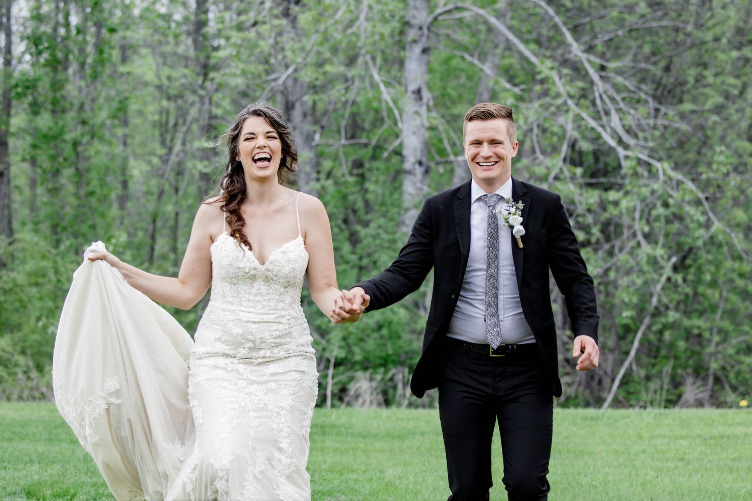 Wedding couple laughs together against natural woodland backdrop with spring greenery.