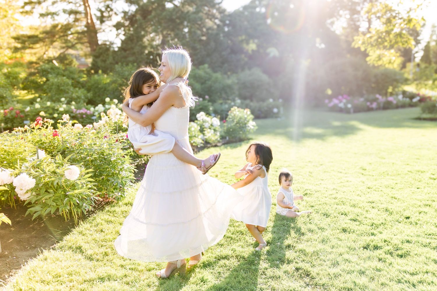 Sunlit outdoor family moment in garden with white summer dresses.