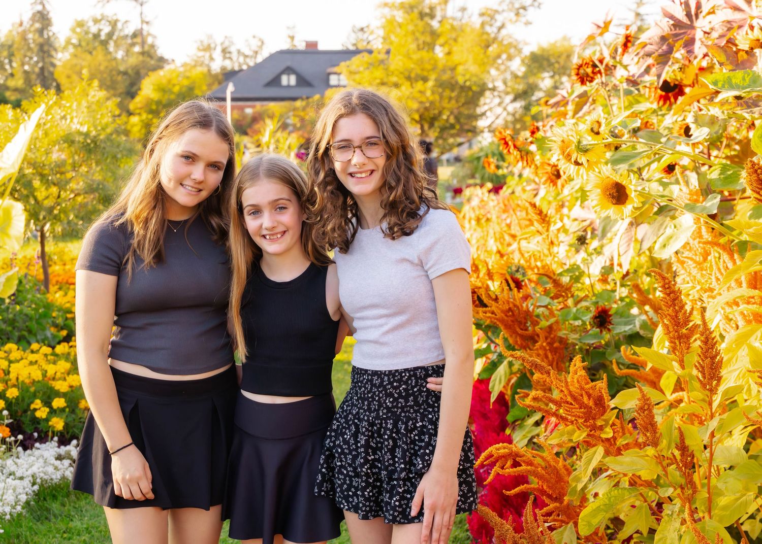 Friends pose together in a garden with vibrant autumn colors and red flowers in the background.