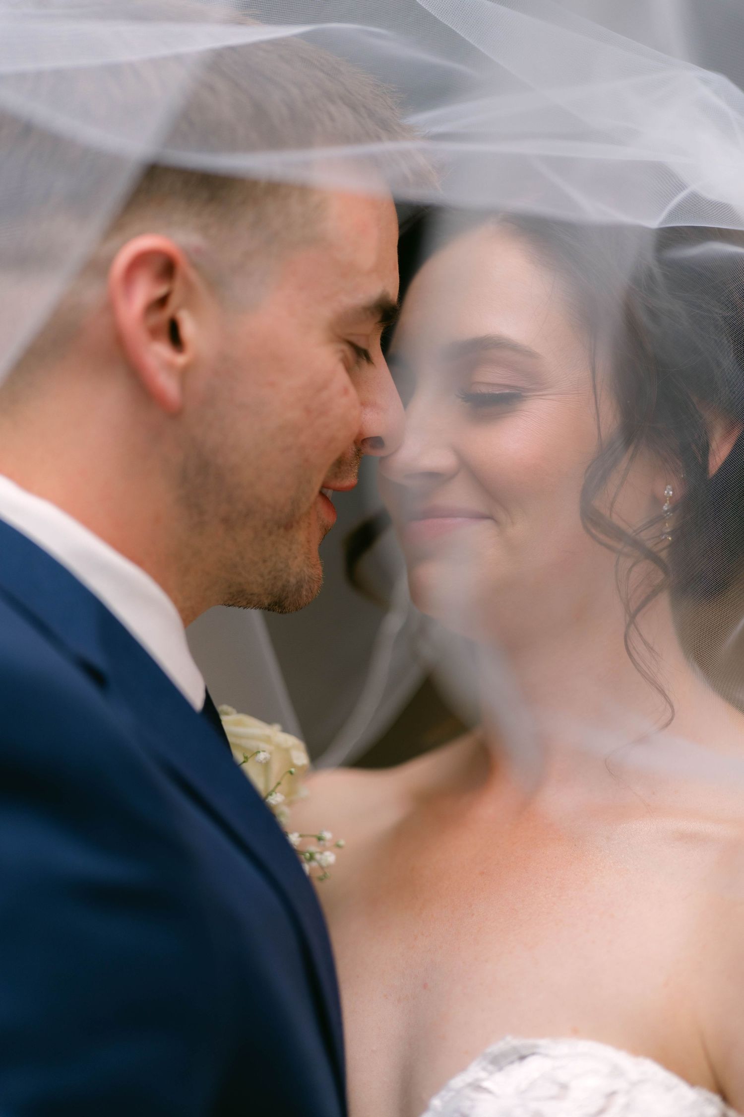 Bride and groom share an intimate forehead touch under a flowing white wedding veil.