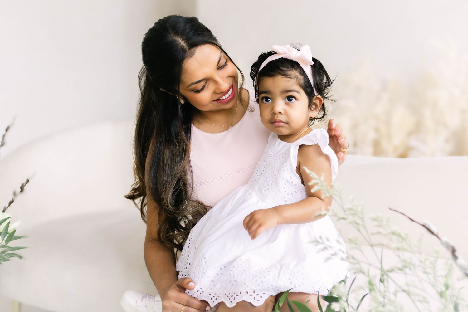 A mother and child share tender moments in white outfits during an outdoor portrait session with soft lighting.