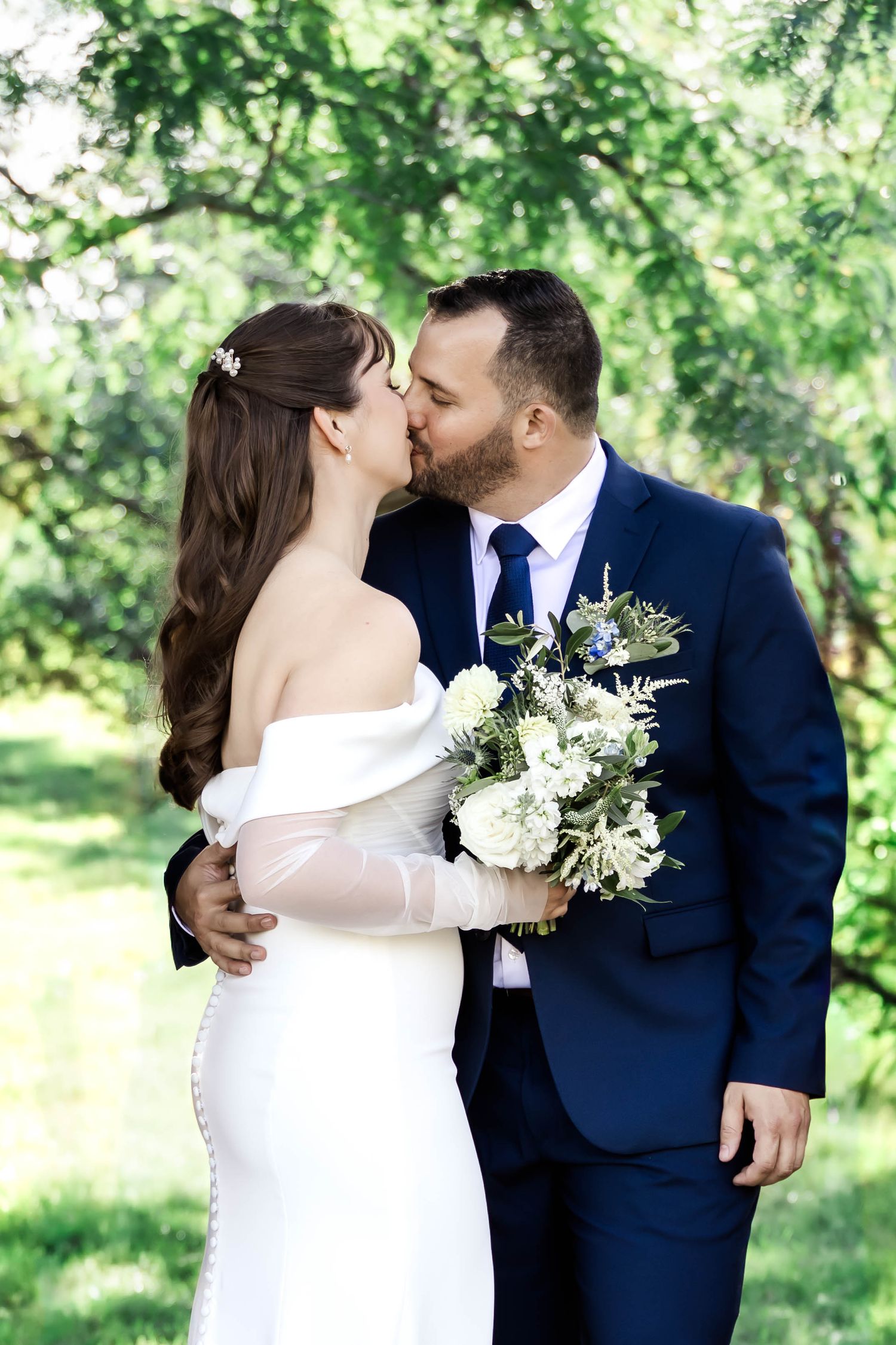 Intimate wedding photography captures tender moments between couple in white dress and navy suit outdoors.