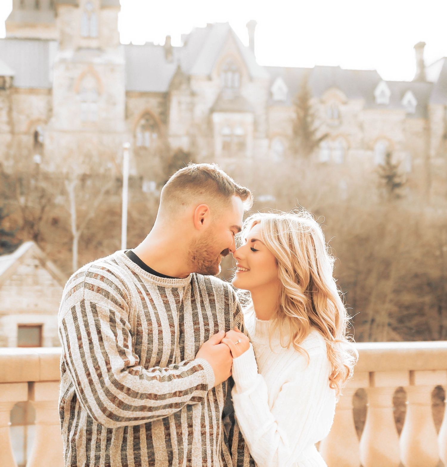 A romantic couple shares an intimate moment on a balcony with a beautiful castle-like building in the background.