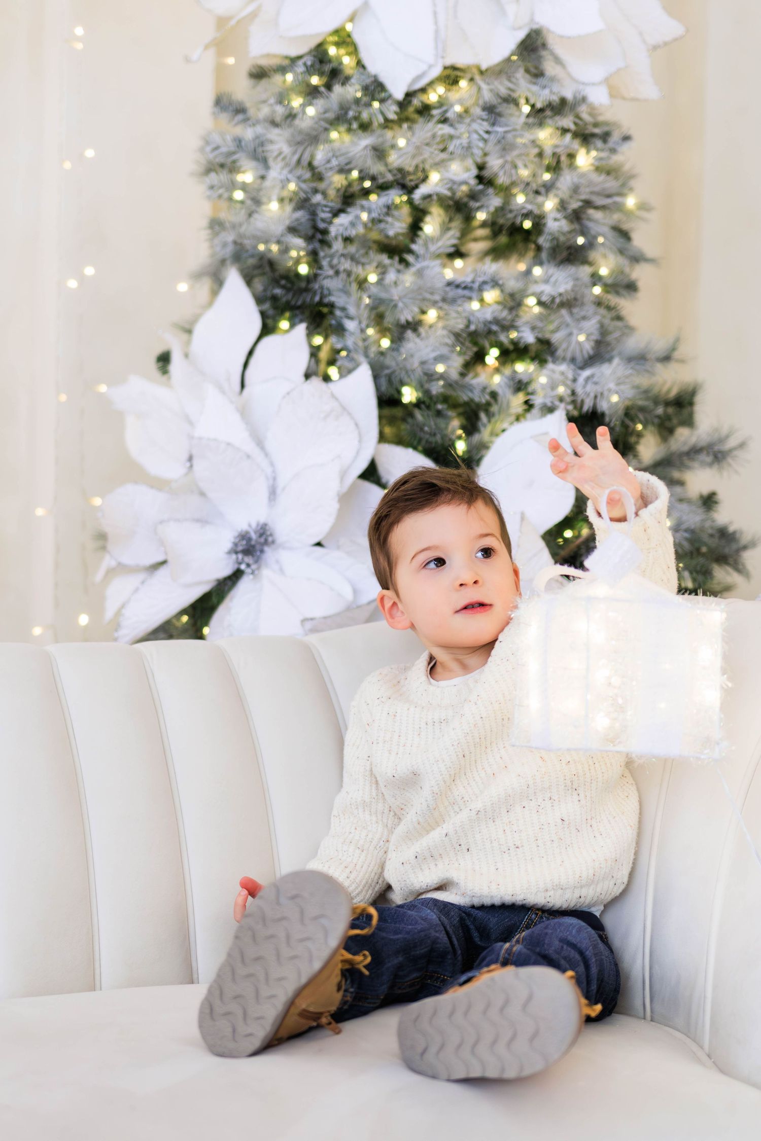 Relaxed pose on white couch with festive Christmas decorations in background.