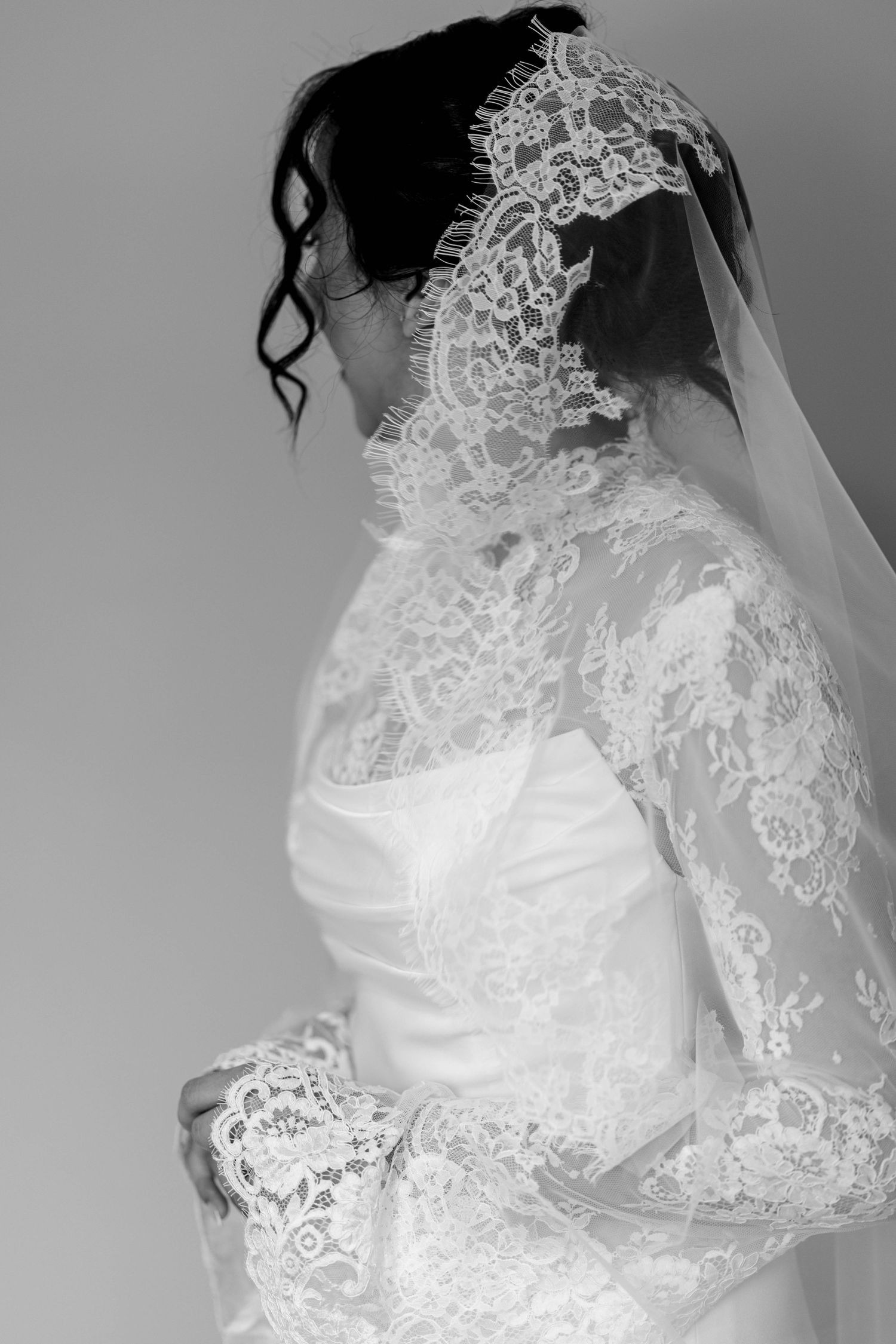 Elegant bride in lace long sleeve wedding gown and veil photographed from behind in black and white.