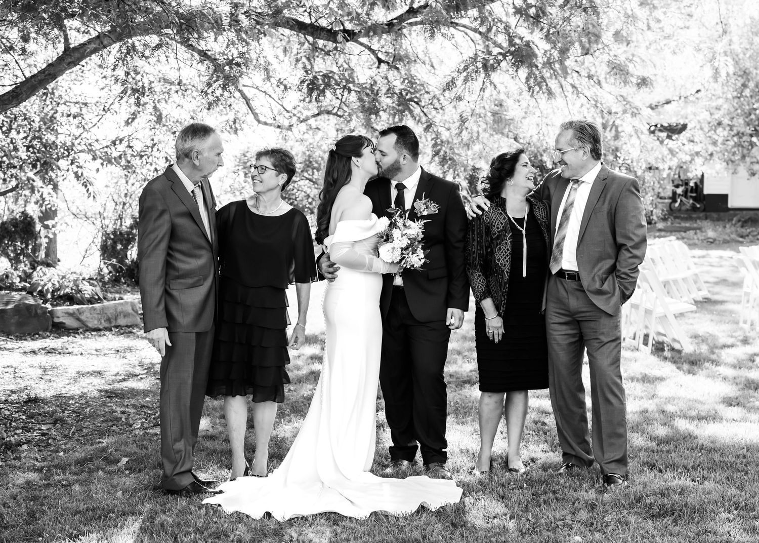 Wedding party and guests gathered under trees for outdoor celebration in black and white photography.