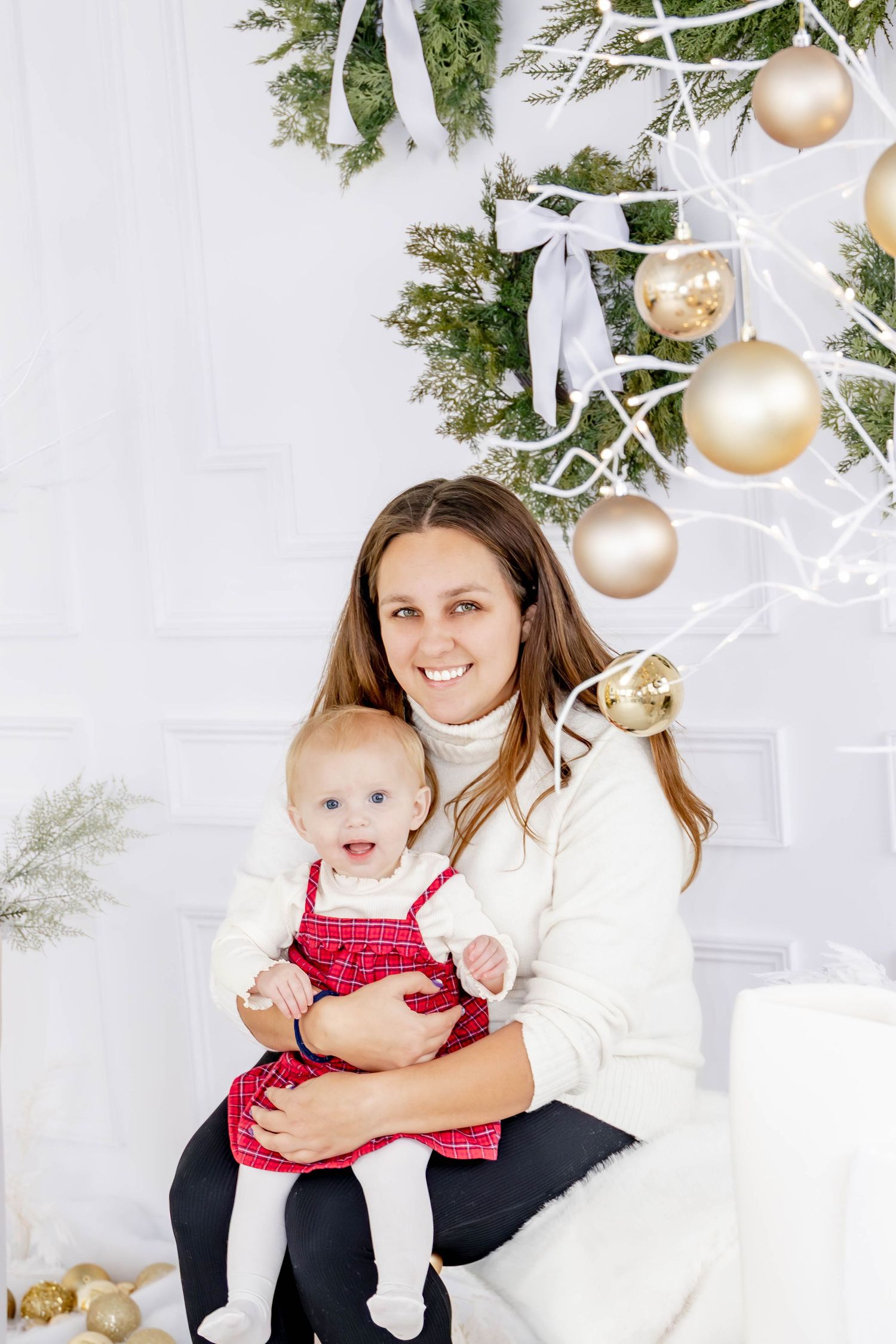 Holiday portrait session with festive wreaths and gold ornaments in white studio setting.