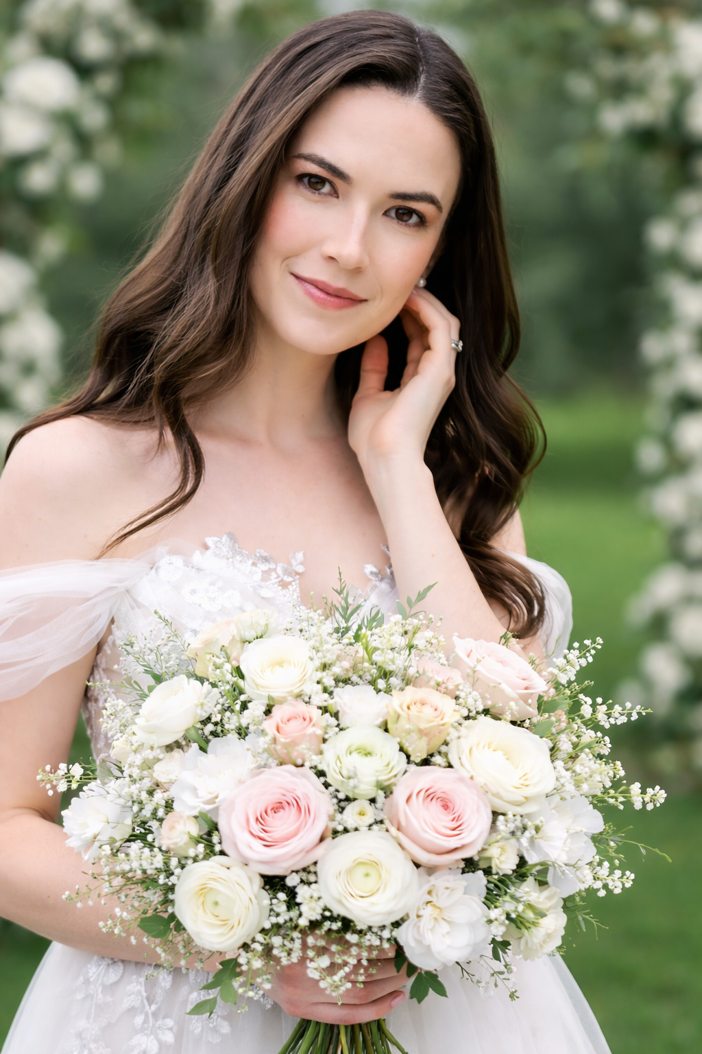 A bride in a white off-shoulder dress holds a romantic bouquet of pink and white roses with baby's breath in a garden setting.