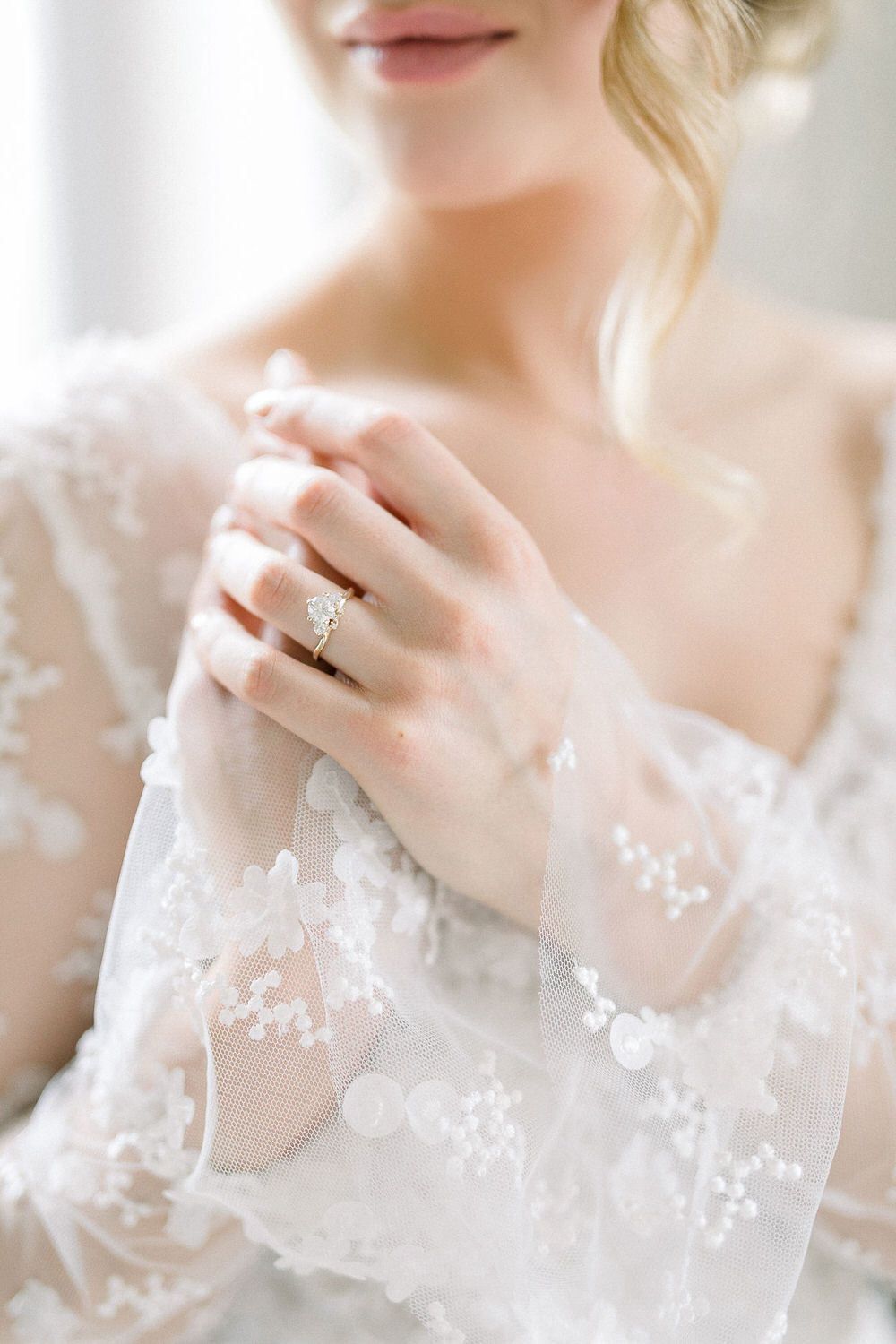 Close-up details of delicate lace sleeves and engagement ring on a bride's hand.