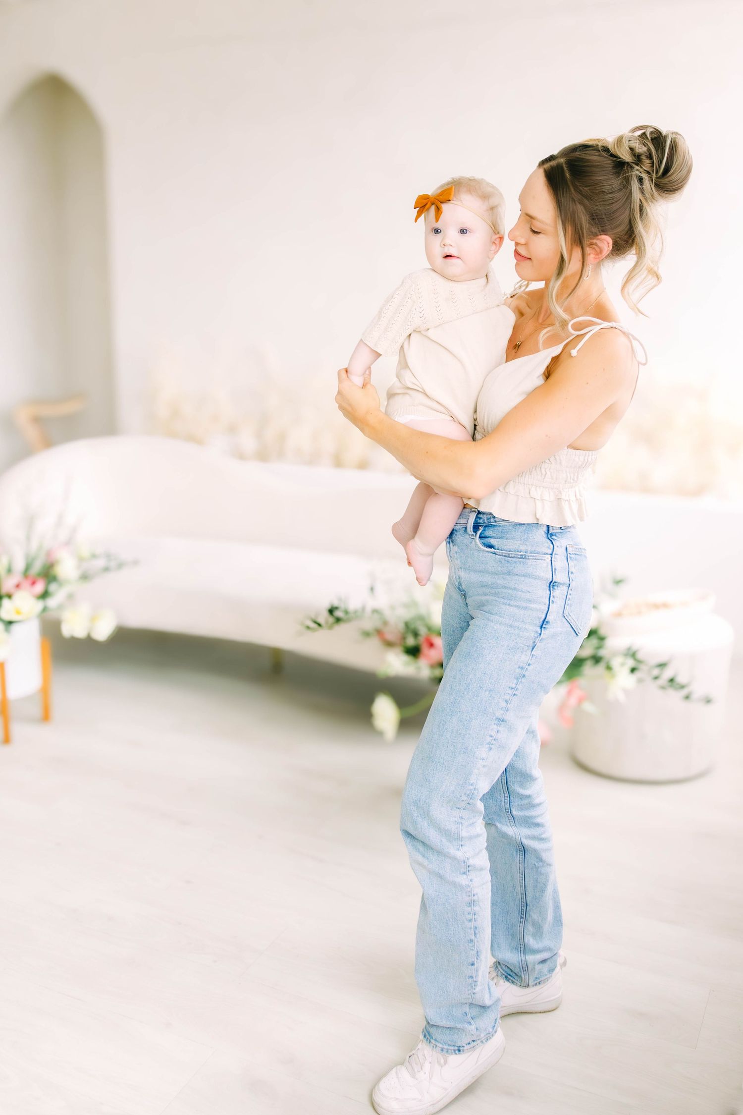 Parent and child share a playful moment in a bright white room with floral decorations.