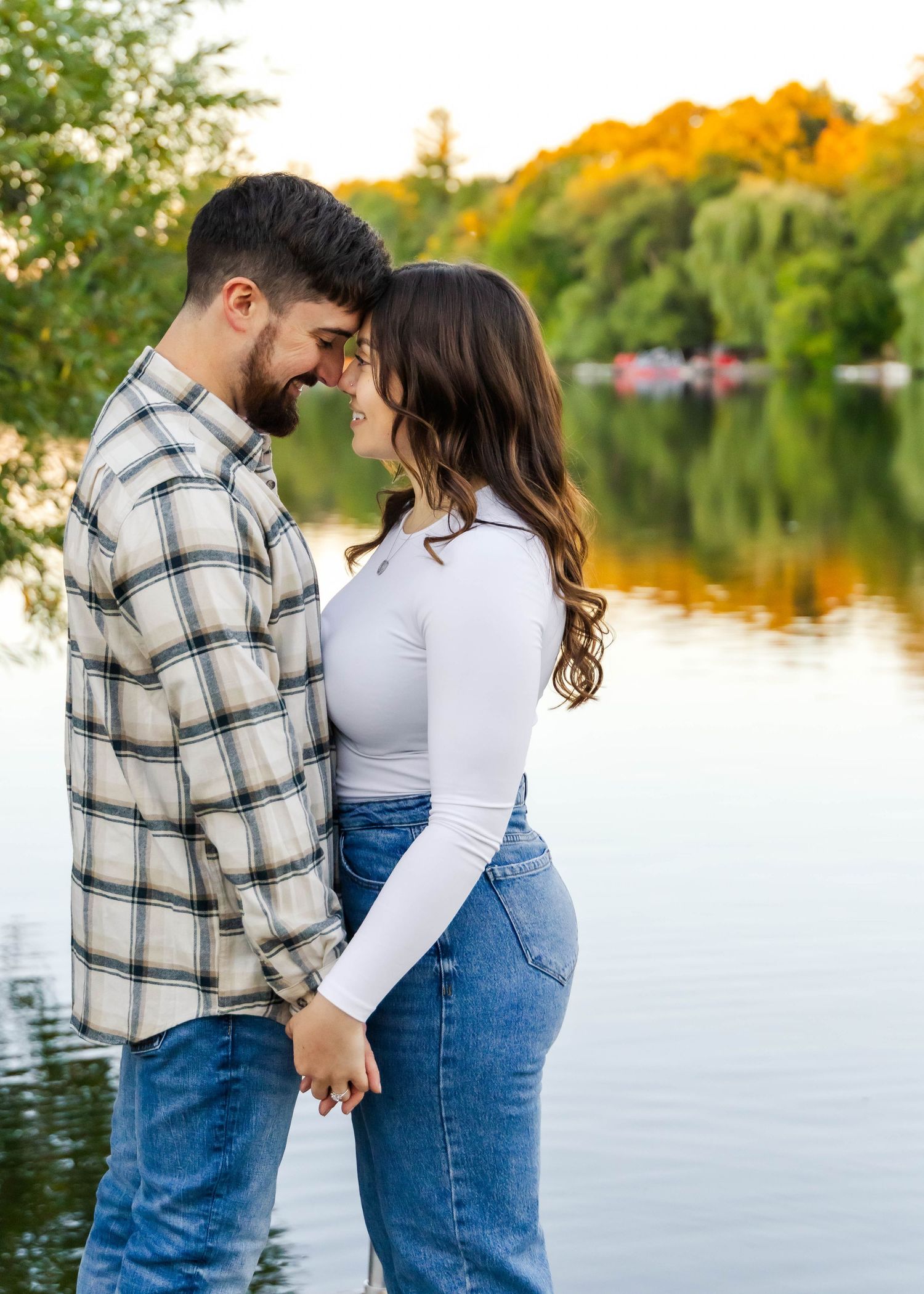 A romantic moment between a couple standing by a lakeside with golden trees in the background.