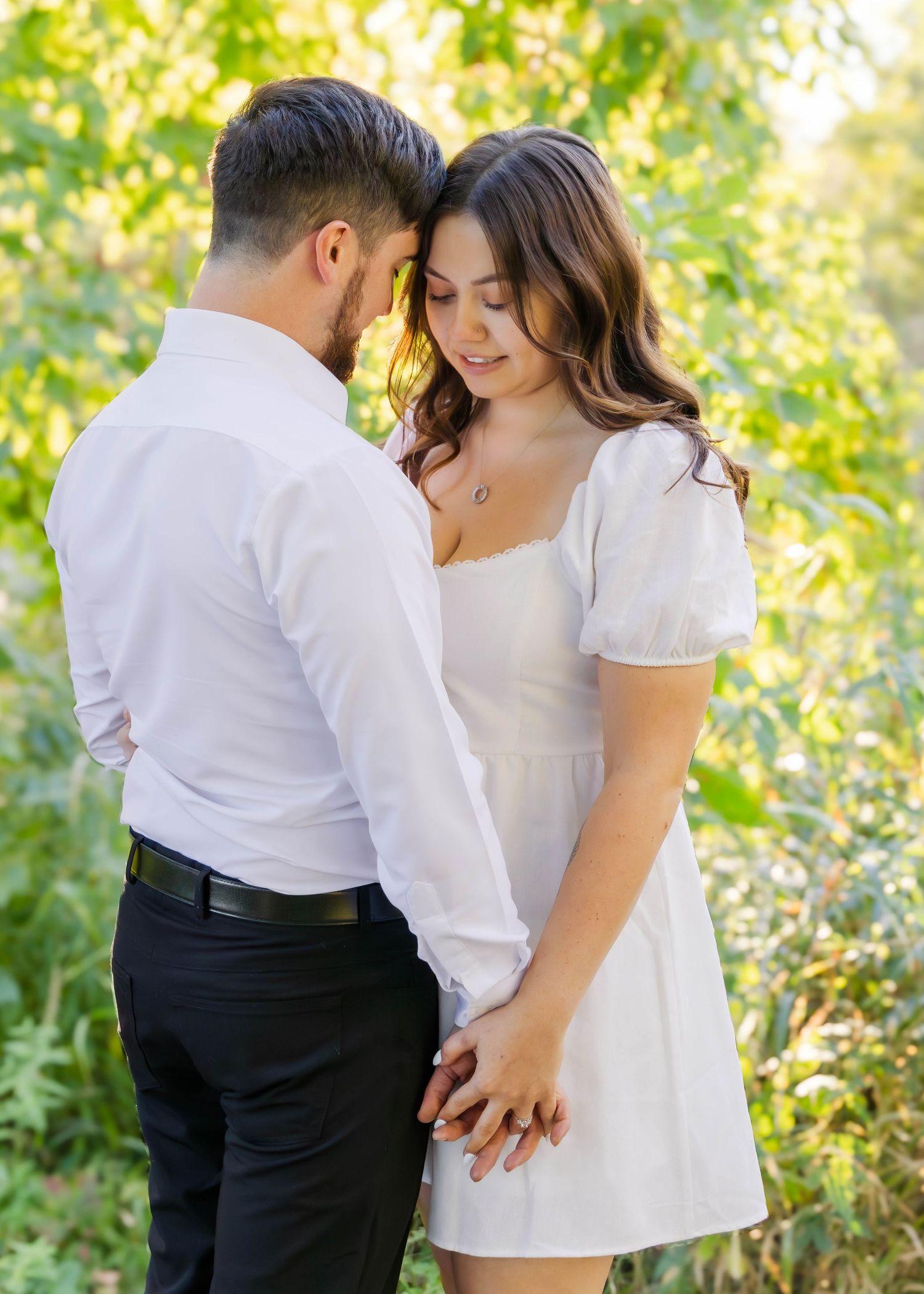 Sweet couple in white outfits share tender moments on a sunlit wooden path.