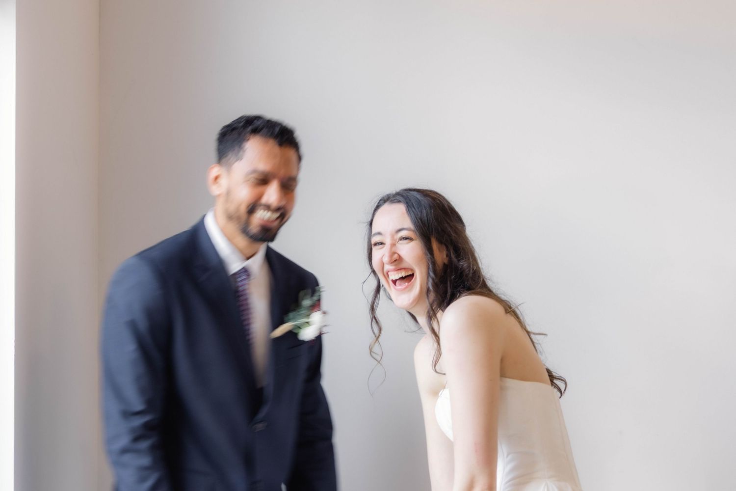Candid indoor portrait of a happy couple laughing together against a light gray wall.