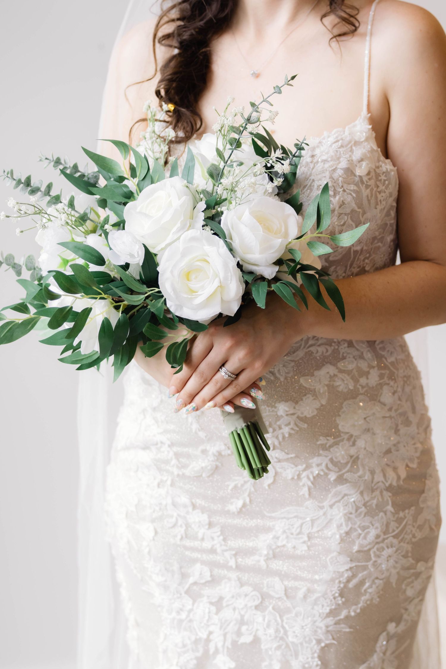 Elegant white lace wedding dress with delicate floral bouquet featuring roses and greenery.