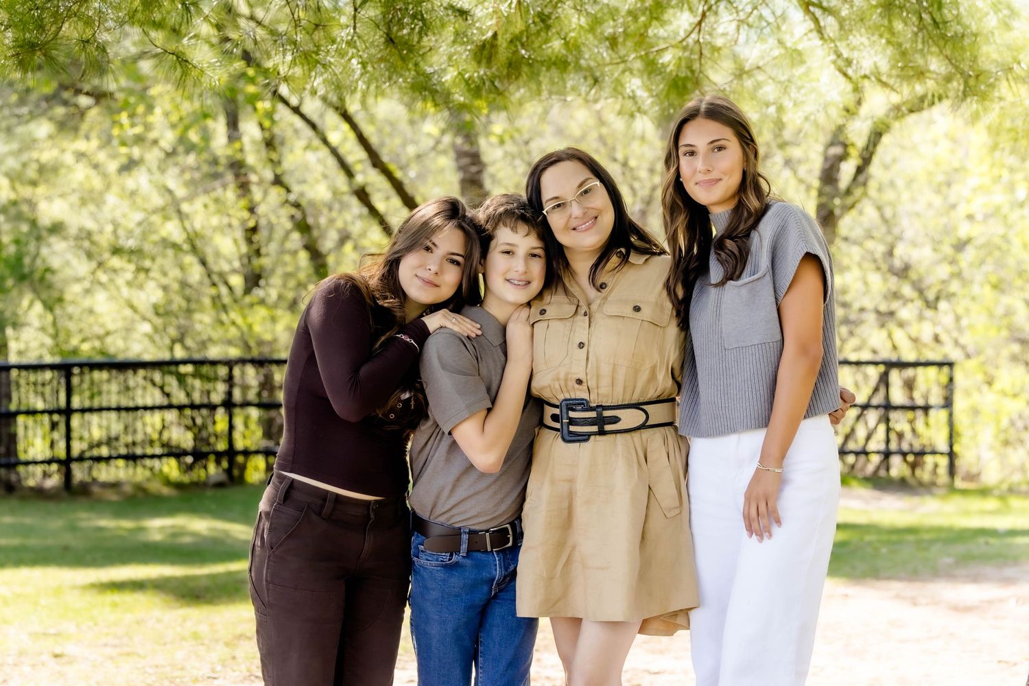 A group stands together with their dogs for portraits under green leafy trees.