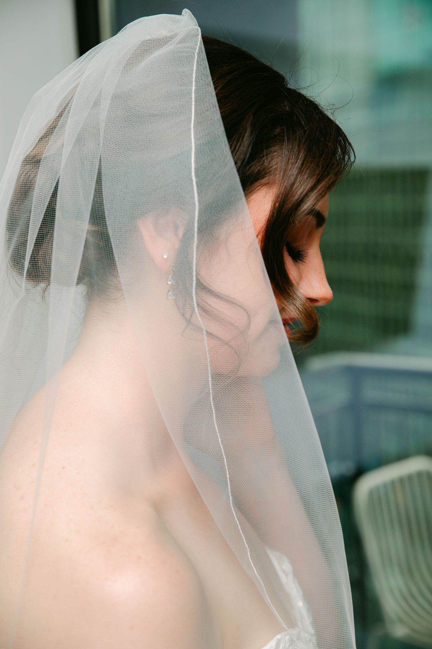 Bride wearing a delicate white veil draped over her head, shown in elegant side profile with pearl earring.