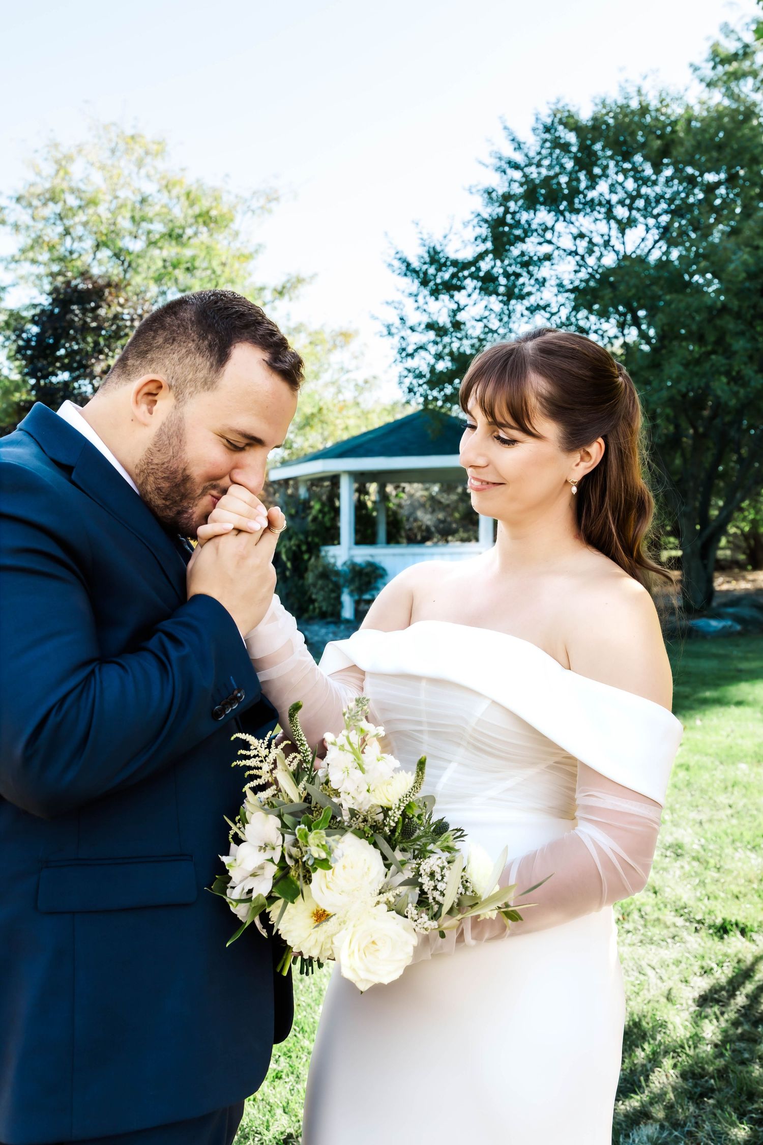 A tender wedding moment outdoors as couple shares an intimate gesture with white floral bouquet.