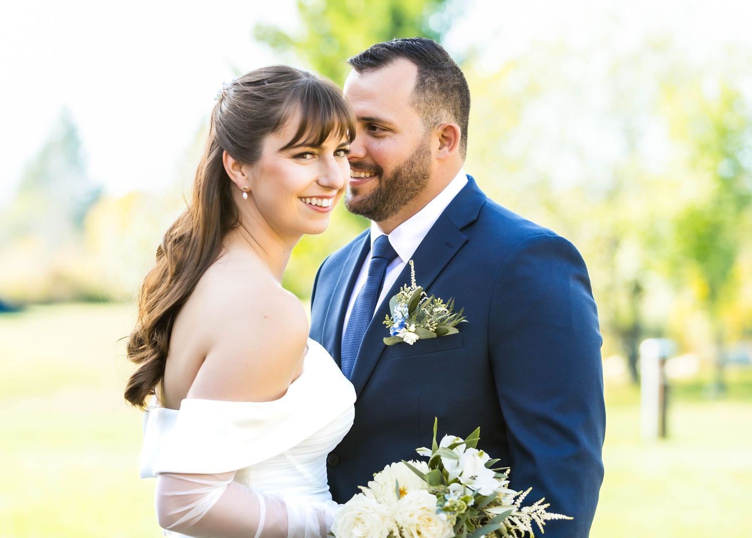 Couple shares a tender moment outdoors surrounded by natural sunlight and greenery.
