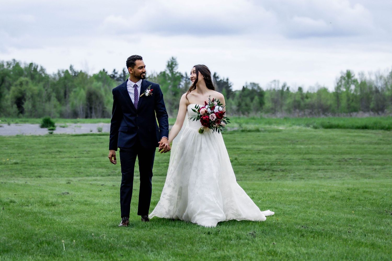 A couple in wedding attire walking through a lush green meadow on their special day.