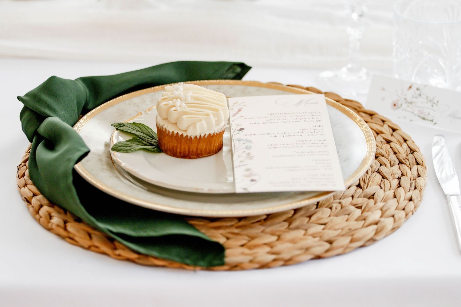Place setting with woven charger, green napkin, and white dinnerware on neutral background.