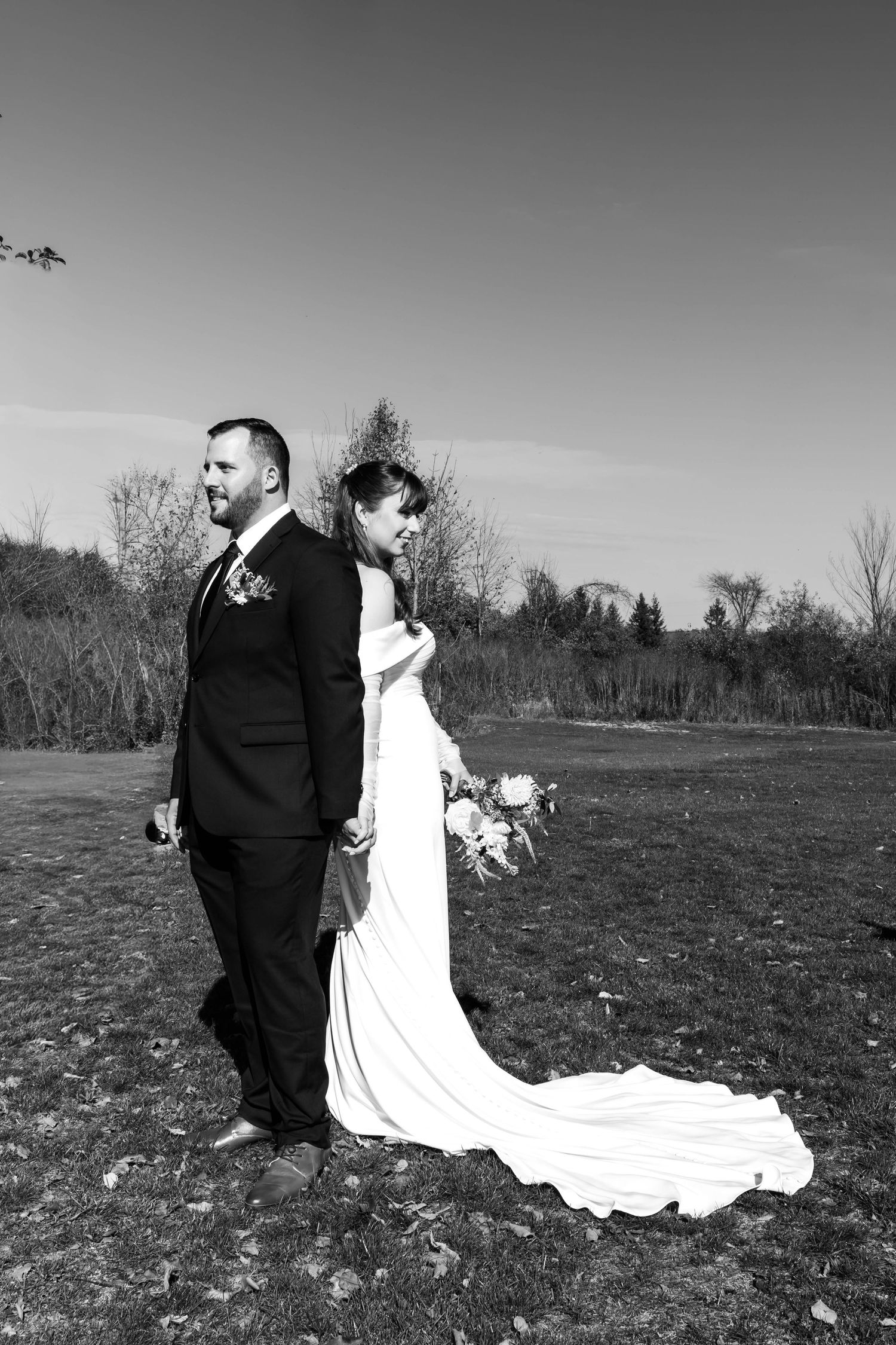 A black and white wedding photo series shows a couple walking through an open field.