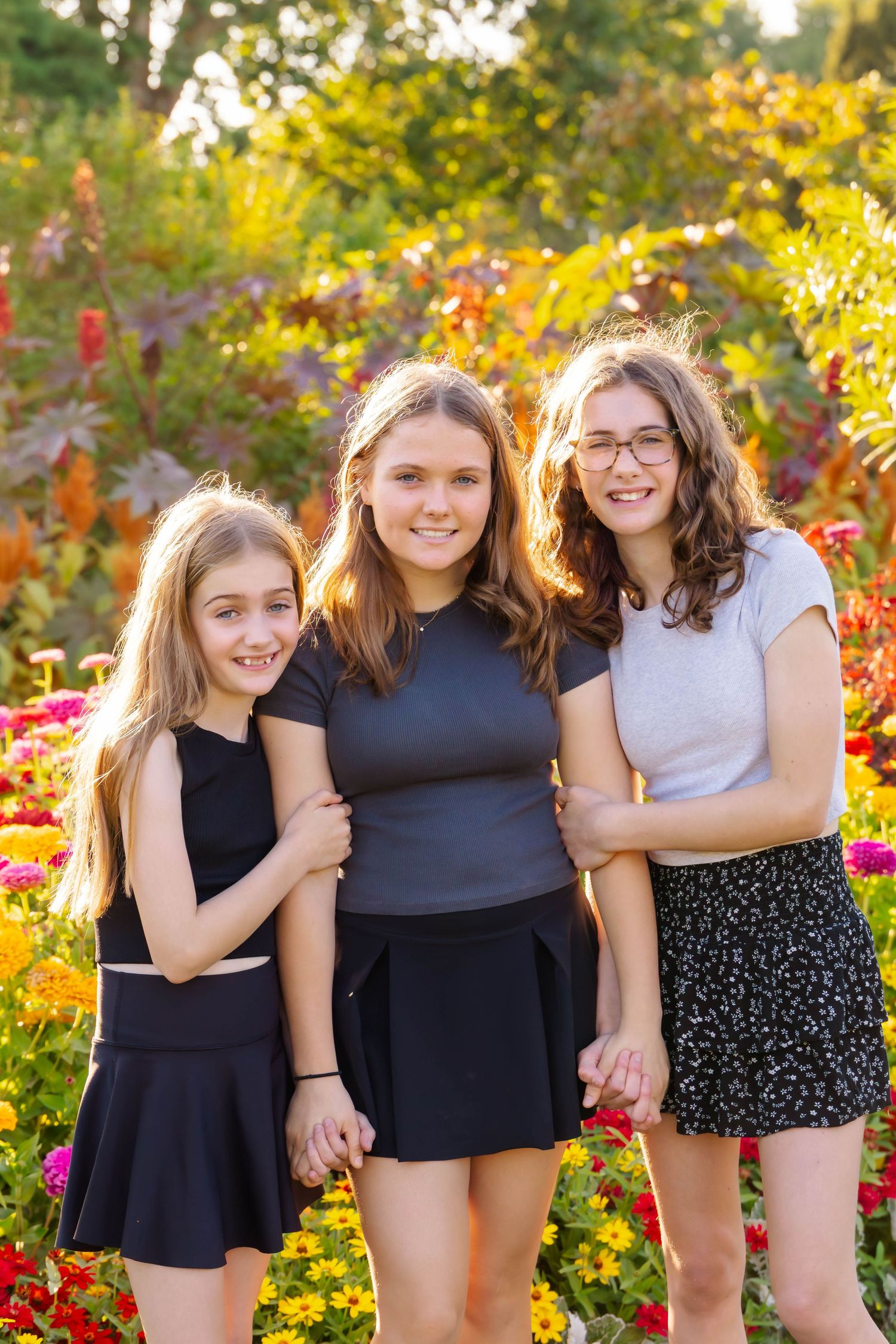 Friends stand together in coordinated outfits against a backdrop of autumn flowers and golden leaves.