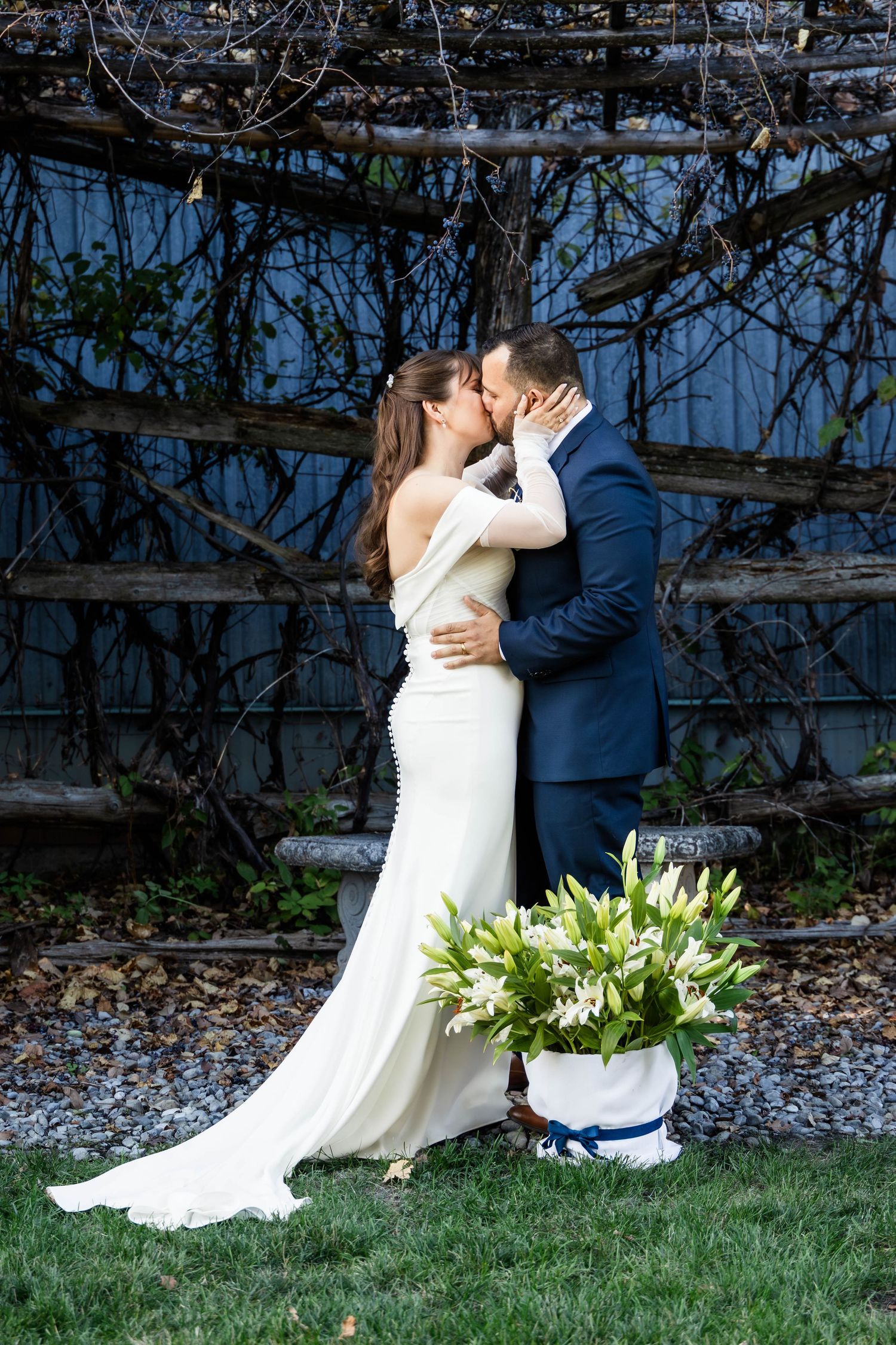Wedding couple shares tender moments near a rustic fence with white floral arrangements.