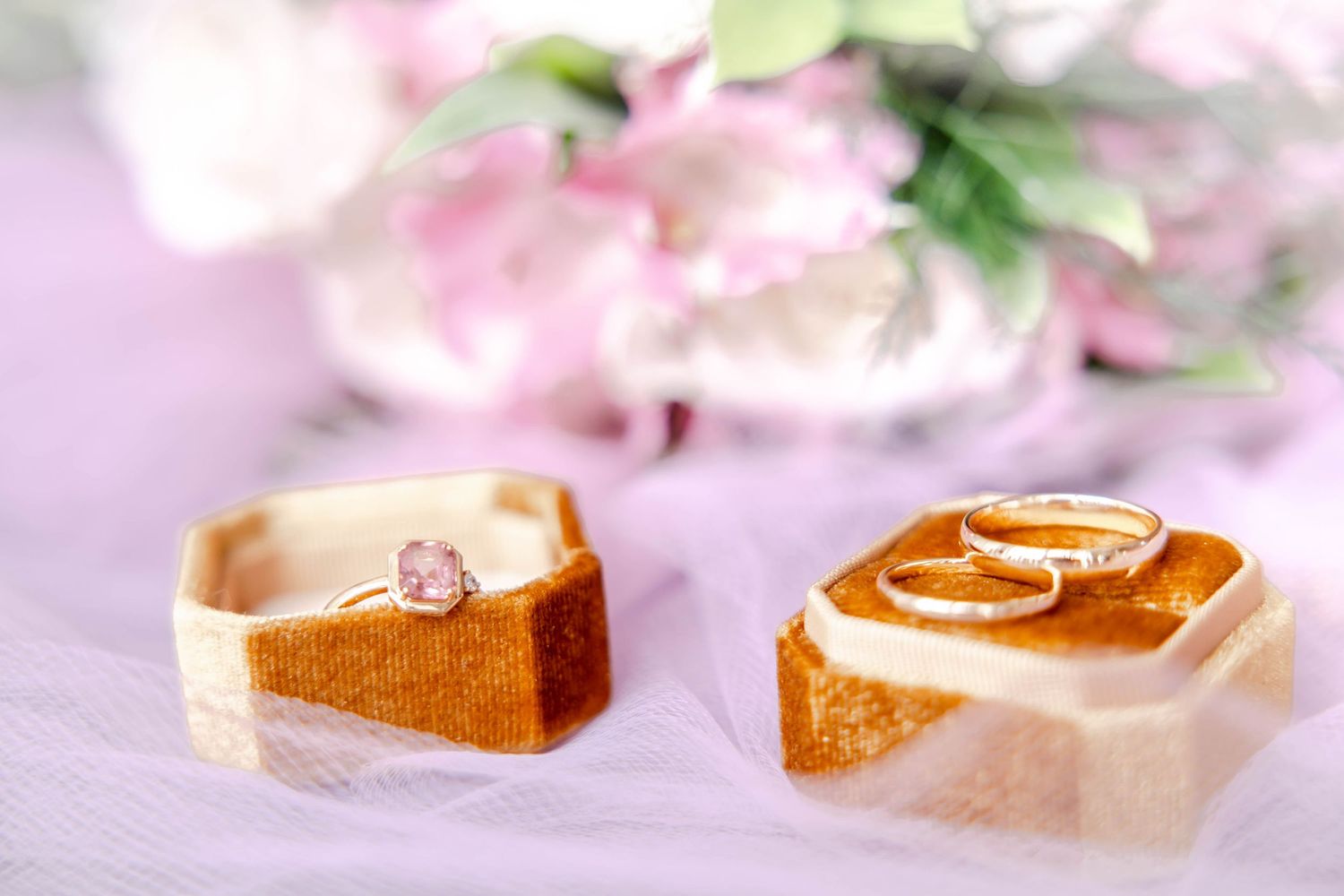 Wedding rings and delicate pink floral decorations arranged on light surface.