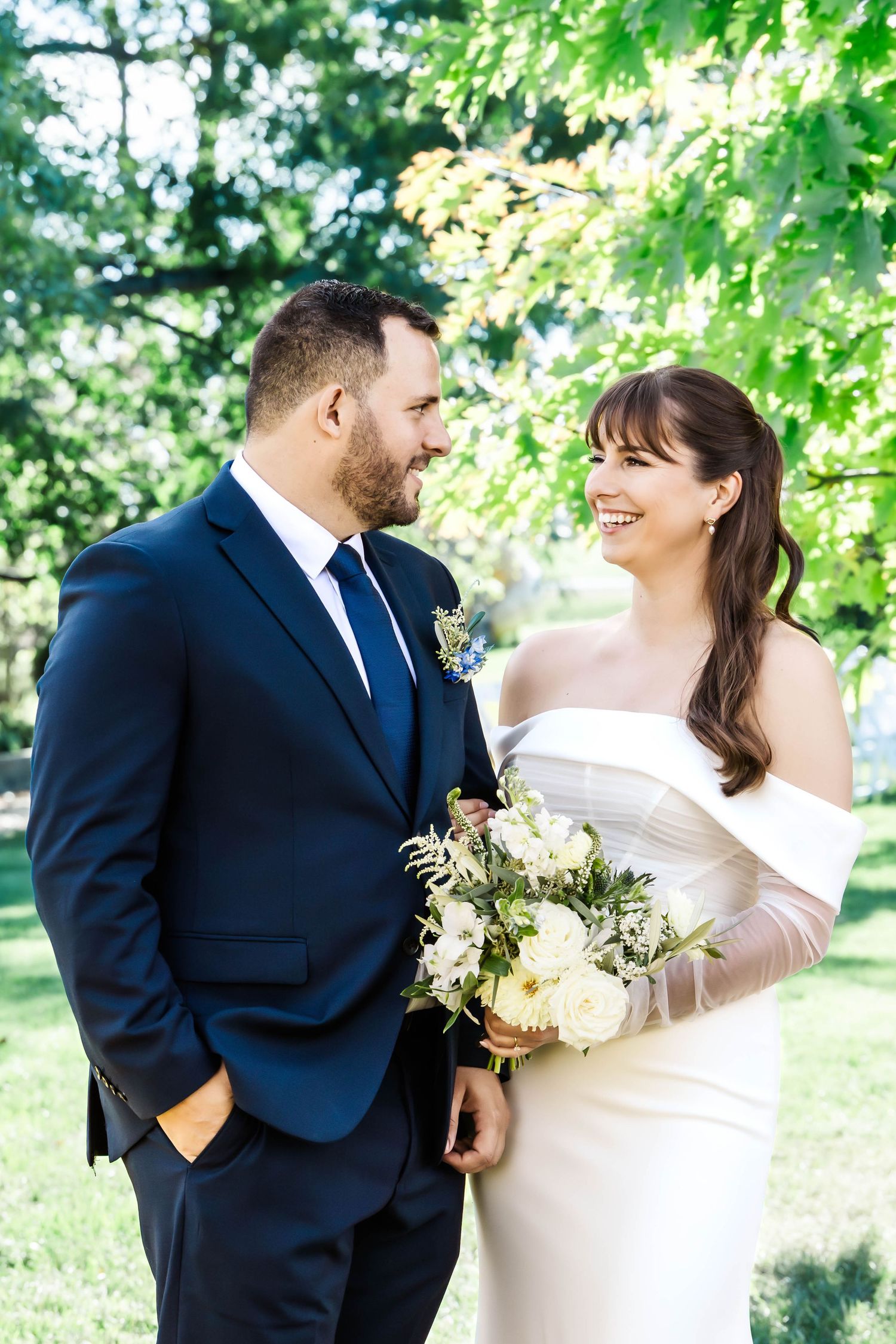 A bride and groom share joyful moments together in a sunlit garden setting during their wedding photoshoot.