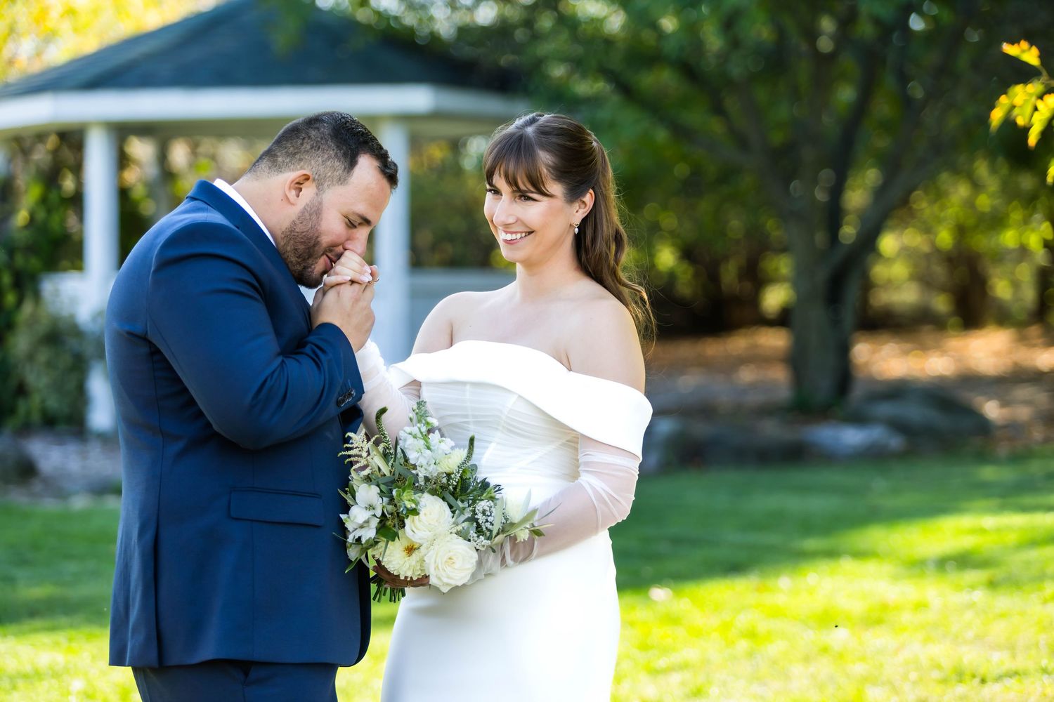 A couple in wedding attire shares a romantic moment in a sunny garden setting with vibrant yellow flowers.