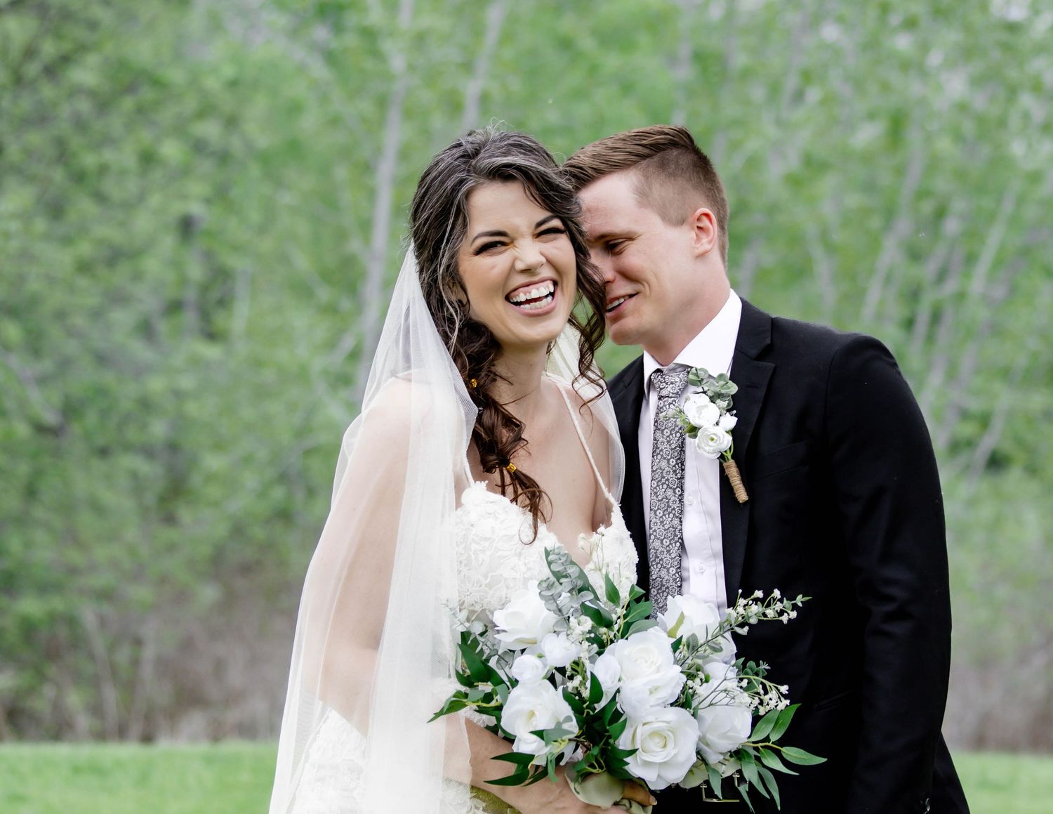 Newlywed couple shares intimate moments outdoors surrounded by greenery in their wedding attire.