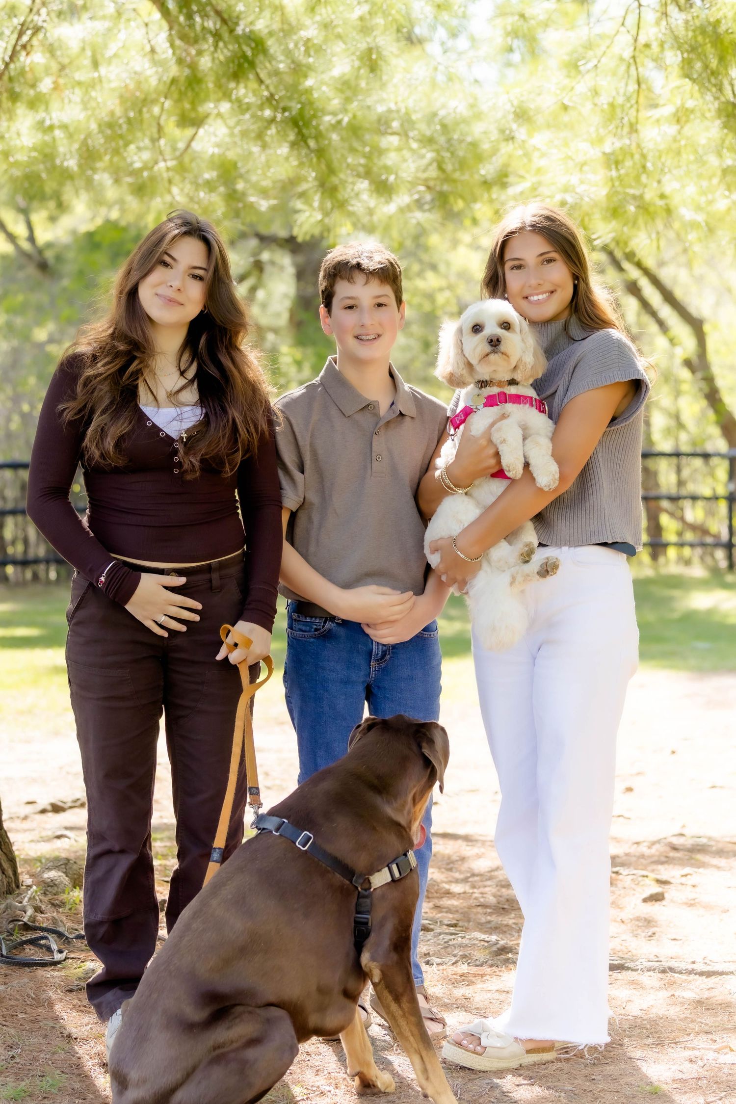 A chocolate labrador and small white dog join their people for outdoor portraits in a park setting.