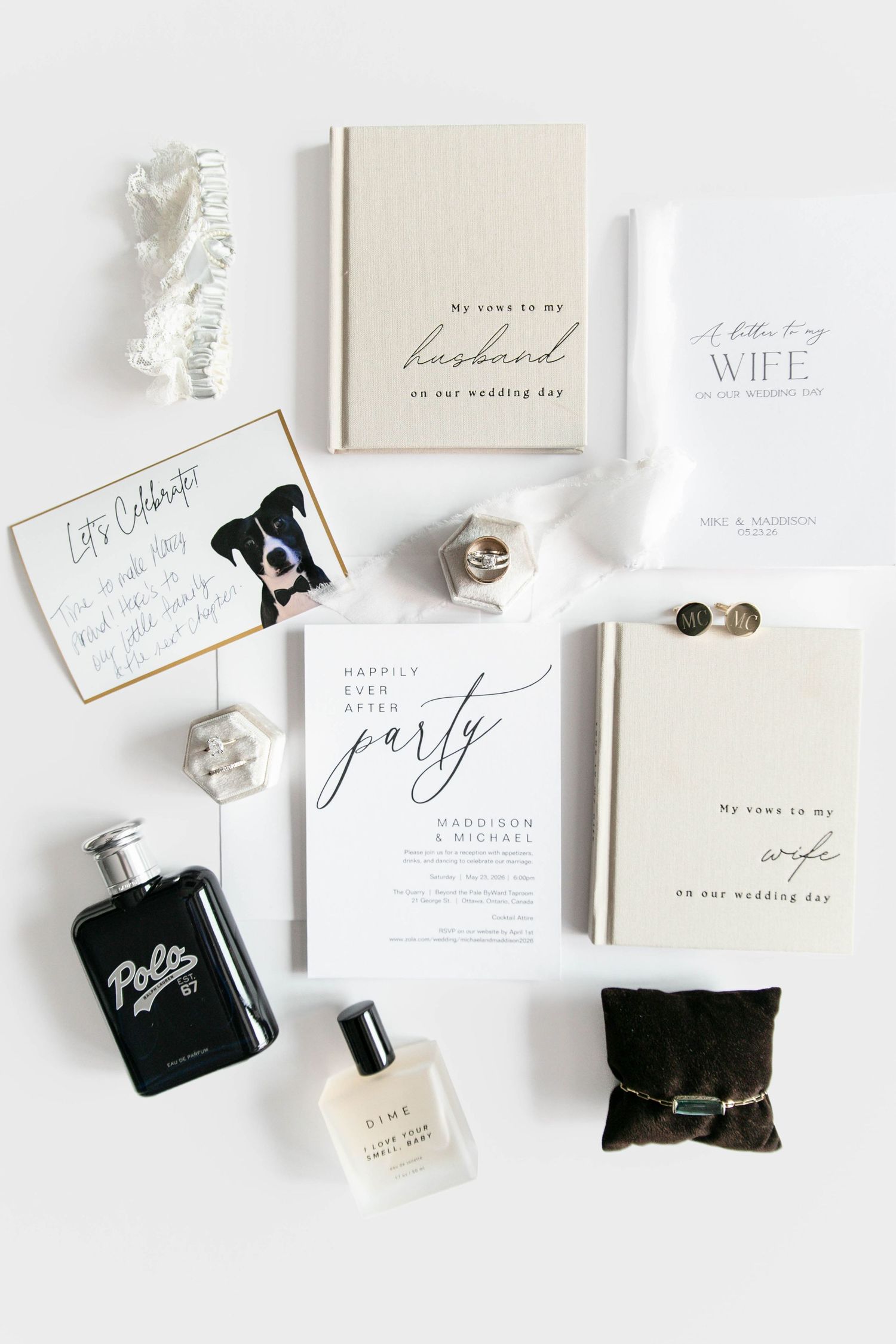 Elegant wedding flat lay featuring vow books, party invitation, cologne, rings, and accessories in black and white palette.