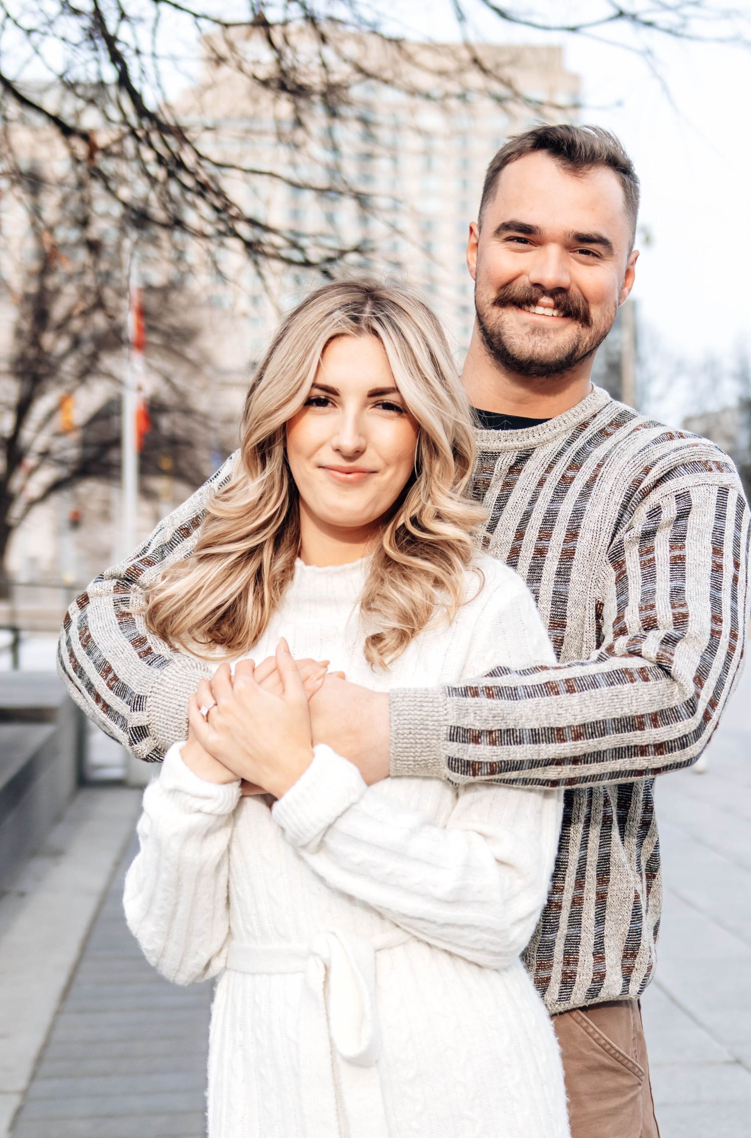 A couple poses outdoors in winter wearing white and striped outfits in a series of candid engagement photos.