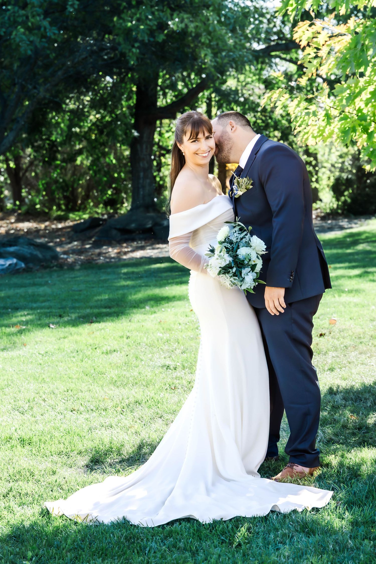 Wedding couple poses together on green grass during an outdoor summer photoshoot.