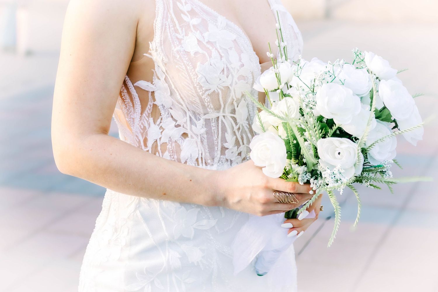 A bride in a delicate lace wedding dress holds an elegant white and green floral bouquet.